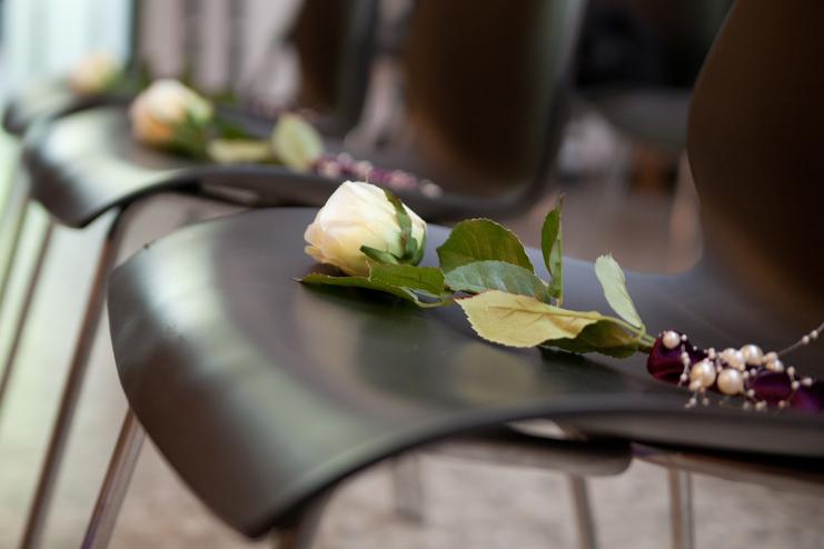 Weißer Rosenbogen mit Blättern und Perlen auf schwarzem Stuhl bei einer Veranstaltung.